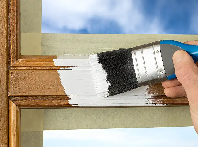 close shot of a persons hand holding a brush painting a taped window frame