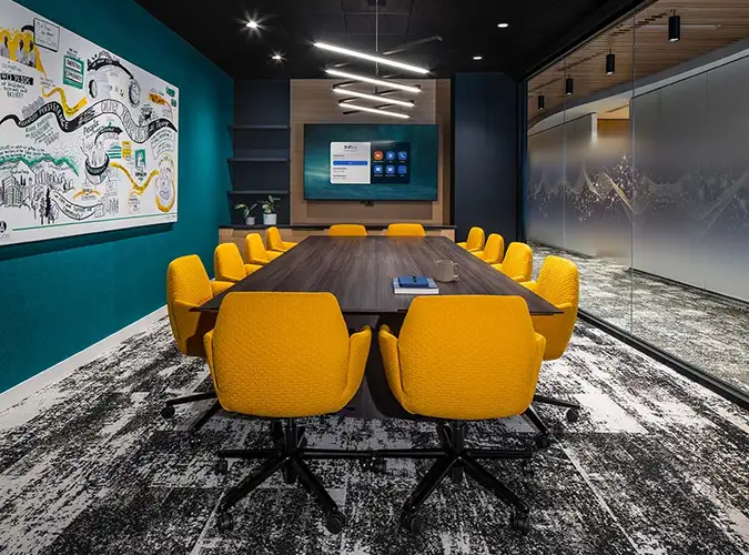 Confernce room with a large table surronded by yellow chairs and gray carpet tile flooring