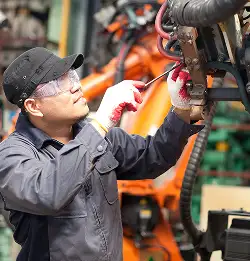 person in workwear wearing safety glasses repairing machine