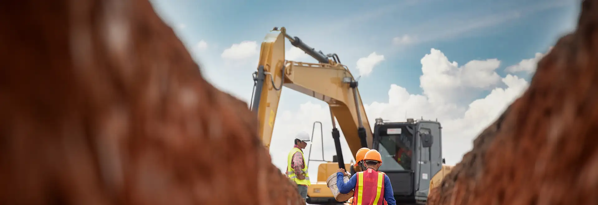 Large machine digging a ditch with workers in hard hats