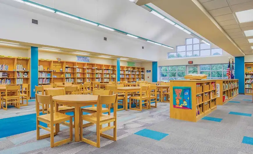Library with light wood shelves and furniture gray carpet tile with insets of teal blue