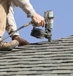 person nailing shingles to residential roof with nail gun