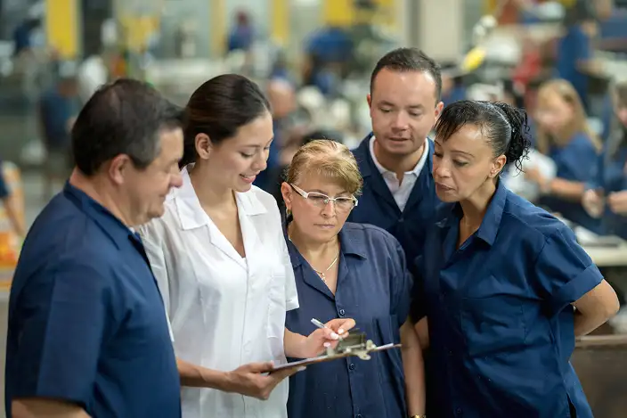 Group of associates on a plant floor looking at a clipboard and smiling