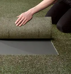 Person pulling back a carpet tile to show Tractionback carpet backing