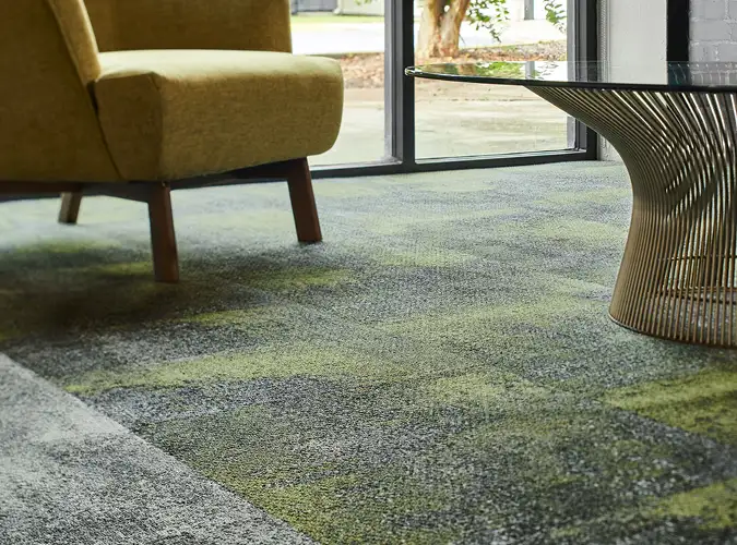 Close up of seating area with green chair on textural carpet tile flooring with green accents