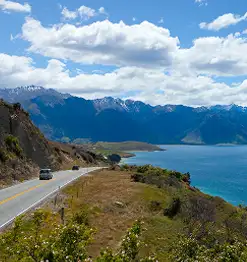 road on moutain next to lake with blue skies and white clouds