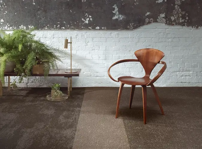 Luxuriuos SDN carpet tile in neutral colors with a chair and plants in front of a painted white brick wall