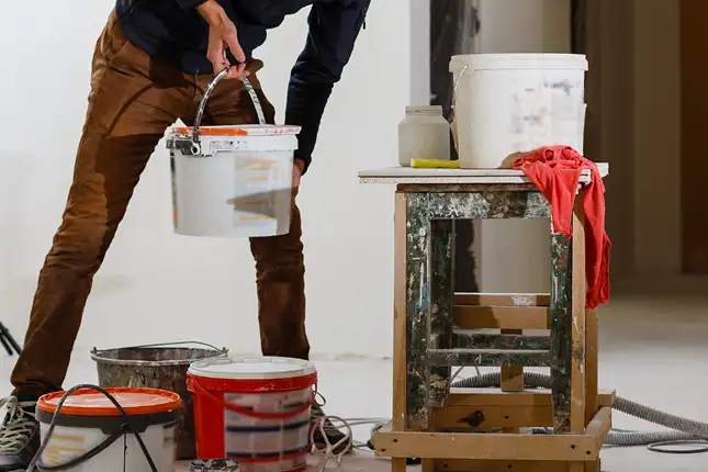 person lisfting paint bucket with several more around a home project