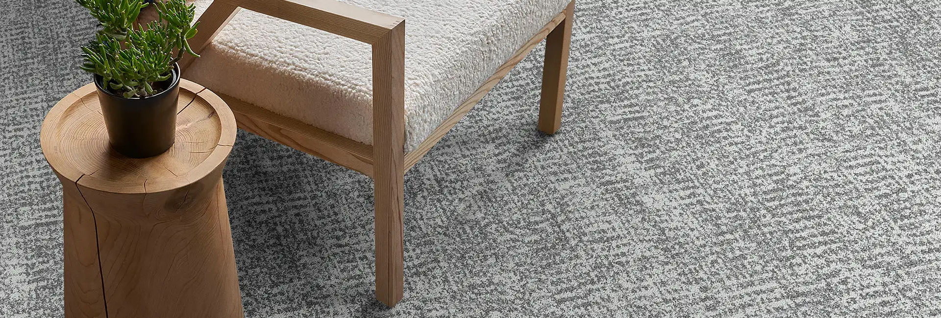 close up of white textured chair with wooden legs and wood side table with plant on neutral textured carpet tile flooring