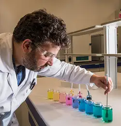Chemist in lab coat and saftey glasses with colored liquids