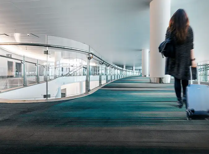 person walking through an airport with wheeled lugage on gray and teal carpet tile