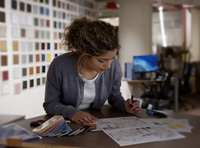 Designer working at a deak with blue prints and color swatches