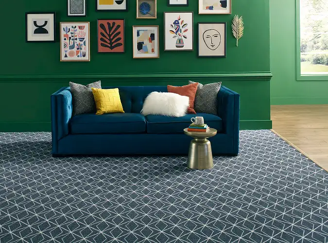 Vibrant interior with art on a green wall and a blue sofa with colorful pillows and geometric carpet if blue and white