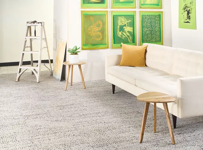 white sofa with yellow pillow in a room with silk screens hanging as art textured carpet tile flooring