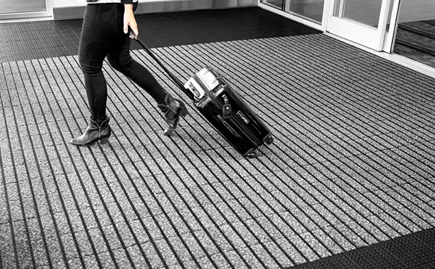 person with rolling bag over OBEX Grid entryway product