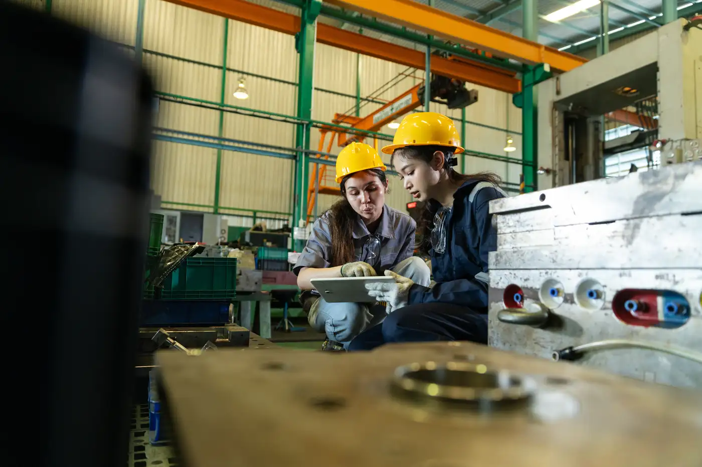 two people on plant floor pointing at a tablet wearing safety gear
