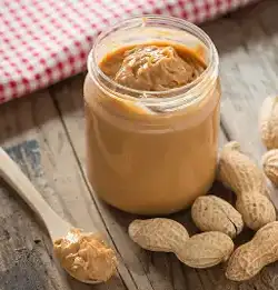 Jar of peanut butter on table with peanuts