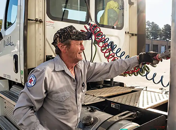 Trucker next to his truck with his hand on the bill of his hat