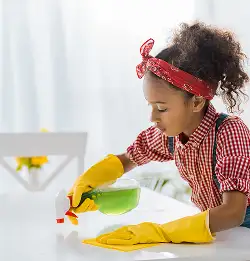 child with rubber gloves on cleaning table with green colored solution in spray bottle