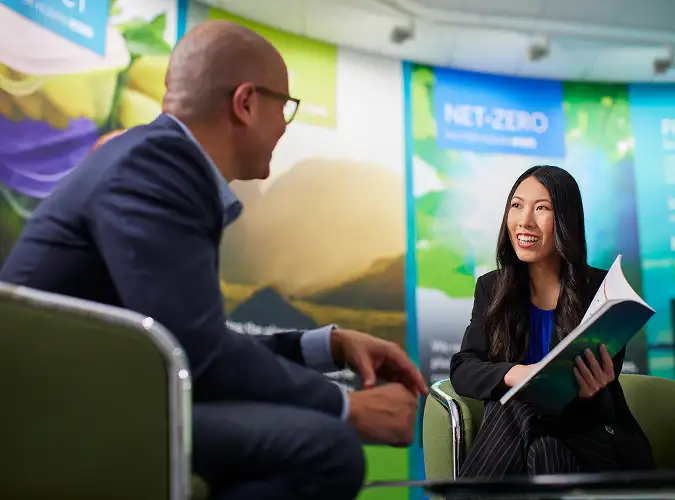 smiling woman presenting to a smiling man with enviormental posters in the background