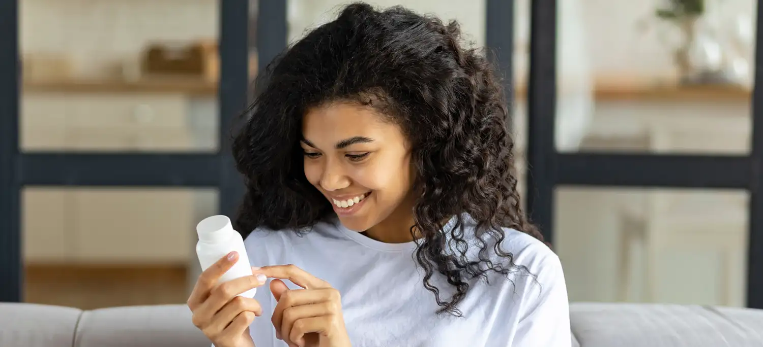 smiling person looking at a white plastic vitamin bottle