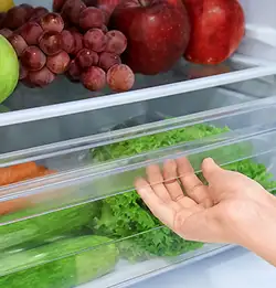 close photo of an opened refigerator showing clear shelves and food drawer 