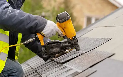 person using nail gun to install shingles on roof