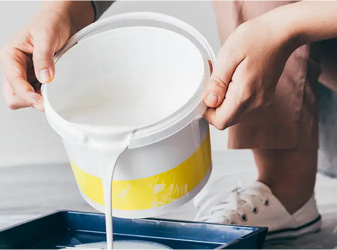 close shot of a person pouring white paint from a buck into a tray