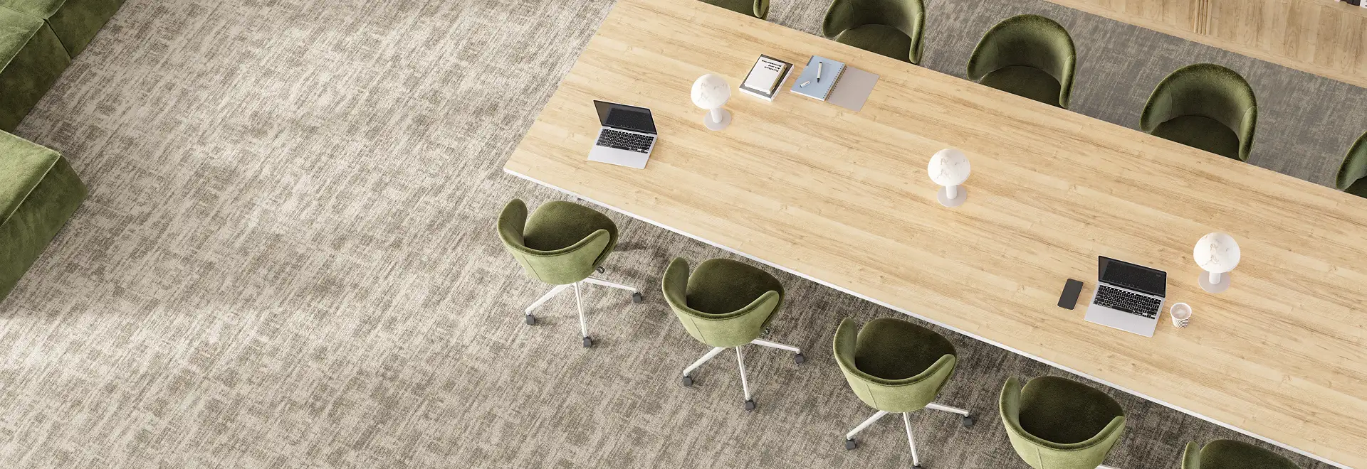 light wood meeting table surrounded by green chairs on tan textural carpet tiles