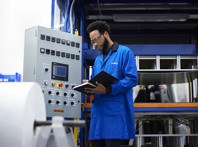 associate standing next to a cotrol panel with safety glasses looking at notebook