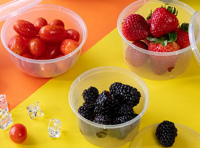 clear food containers with strawberroes blueberries and cherry tomatoes on colorful background