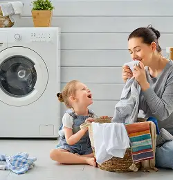 Mother and child in laundry room smiling and smelling fresh clothes