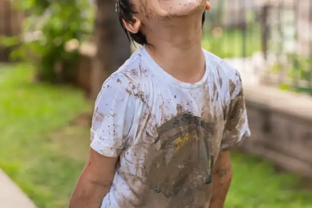 child wearing a white shirt with mud all over it 