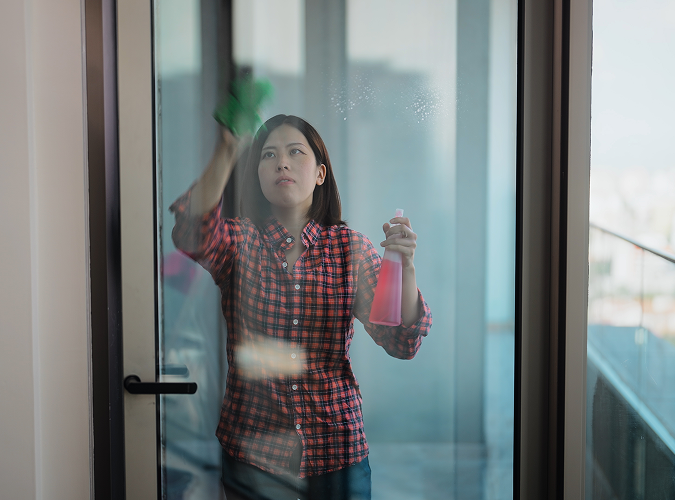 person cleaning a window with colorful cleaner in bottle