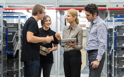 woman with a clipboard speaking withg thre other people on the plant floor