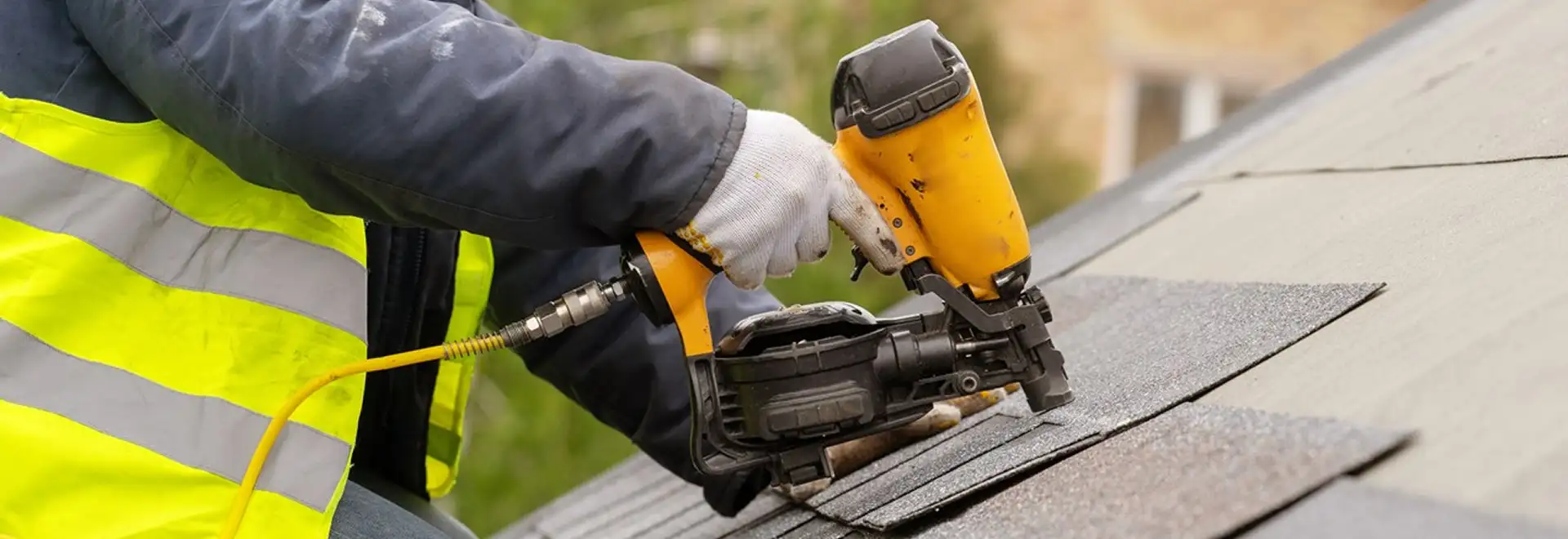 close shot of a preson nailing shinles onto a roof with a nailgun