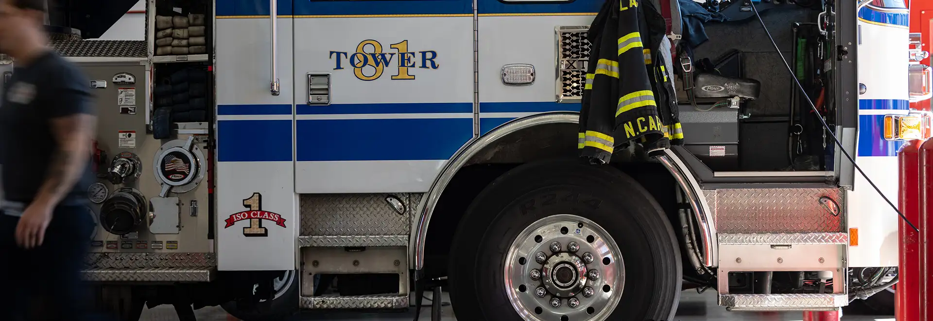 Fire truck in station with a person walking by quickly on the fire truck is turnout gear made with Milliken fabrics